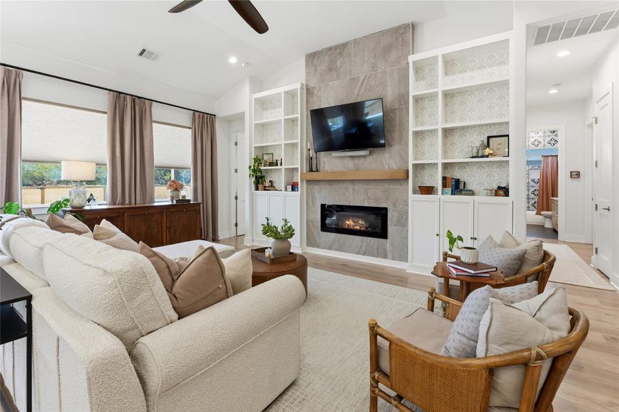 Living area with vaulted ceiling, a ceiling fan, wood finished floors, a tiled fireplace, and recessed lighting