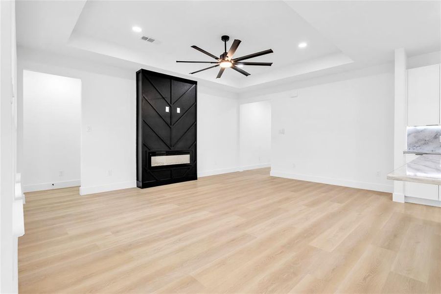 Unfurnished living room featuring light wood-style flooring, ceiling fan, a tray ceiling, and recessed lighting