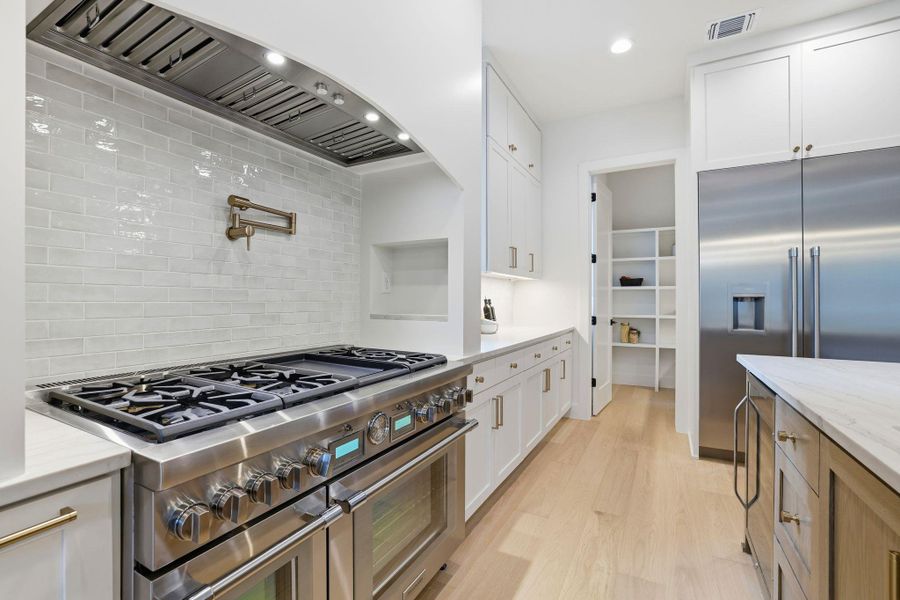 Kitchen with custom range hood, premium appliances, light wood-type flooring, light stone counters, and white cabinets