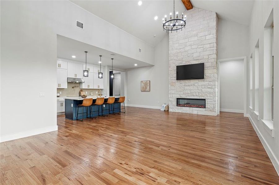 Unfurnished living room featuring high vaulted ceiling, light wood finished floors, a chandelier, beam ceiling, and a fireplace Unfurnished living room featuring high vaulted ceiling, light wood finished floors, a chandelier, beam ceiling, and a fireplace