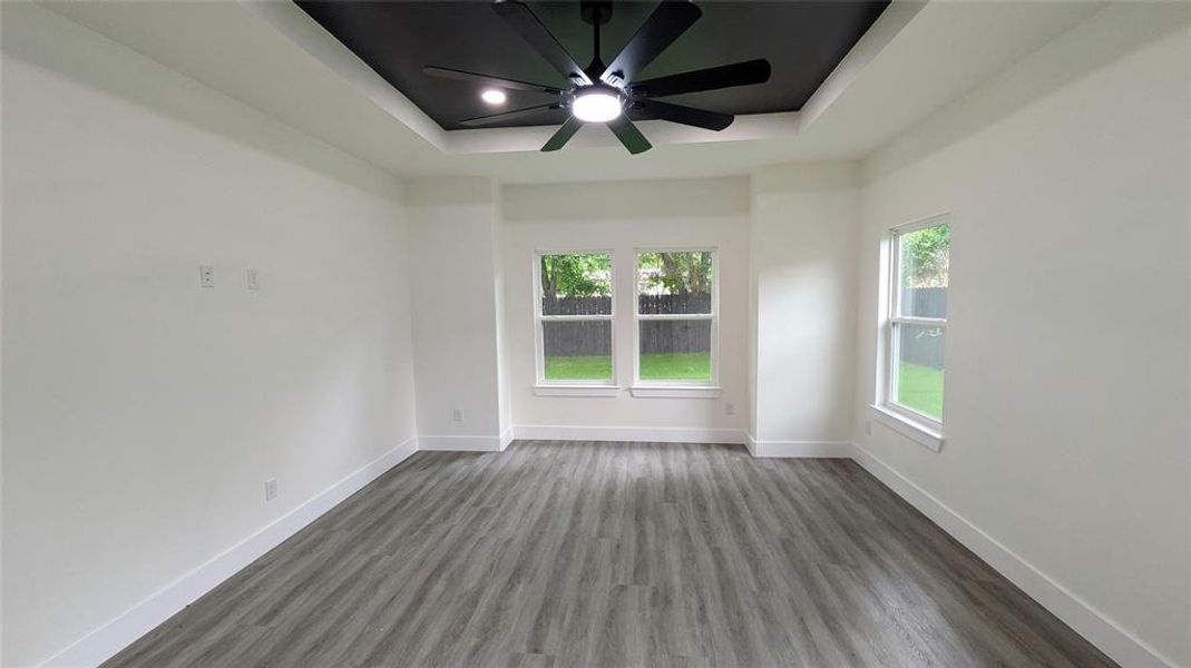 Empty room featuring baseboards, a ceiling fan, a raised ceiling, and wood finished floors