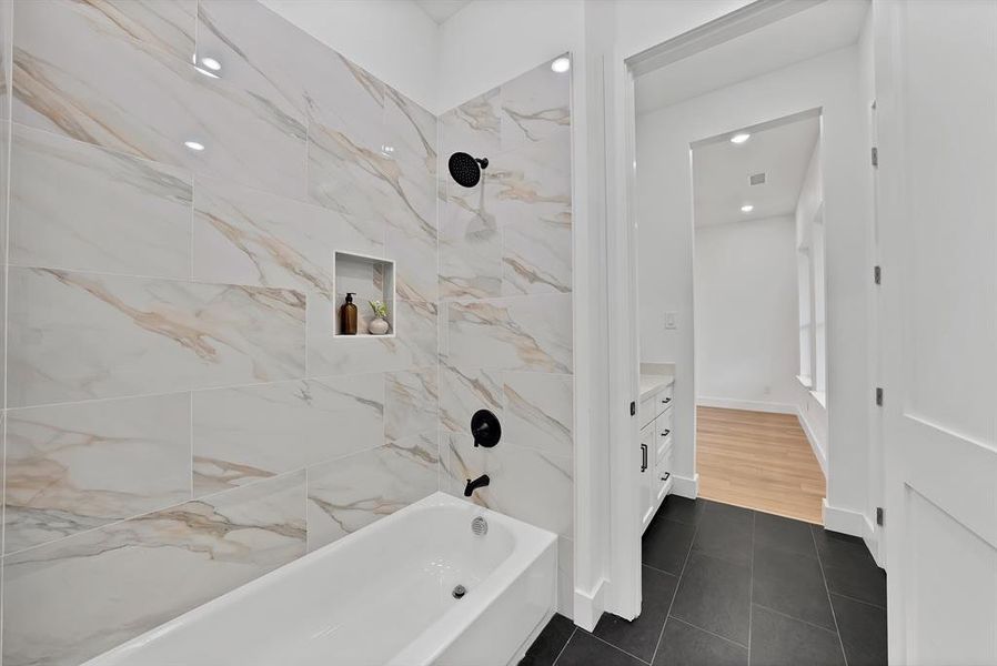 Bathtub with matte black fixtures and a tiled surround featuring a recessed niche
