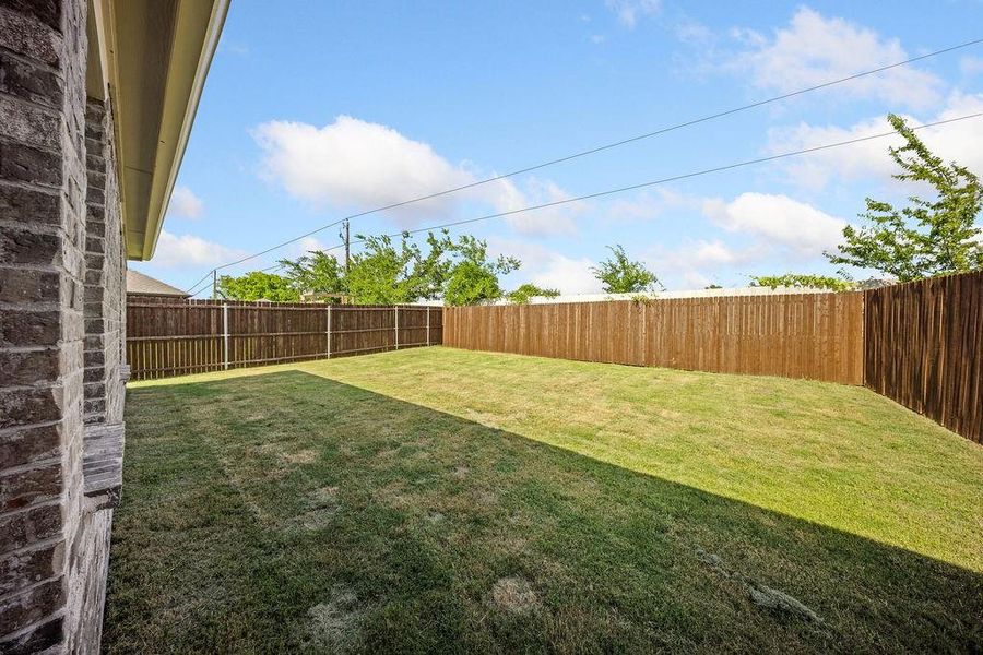 Spacious backyard featuring a manicured lawn, full privacy fencing, and brick exterior Spacious backyard featuring a manicured lawn, full privacy fencing, and brick exterior