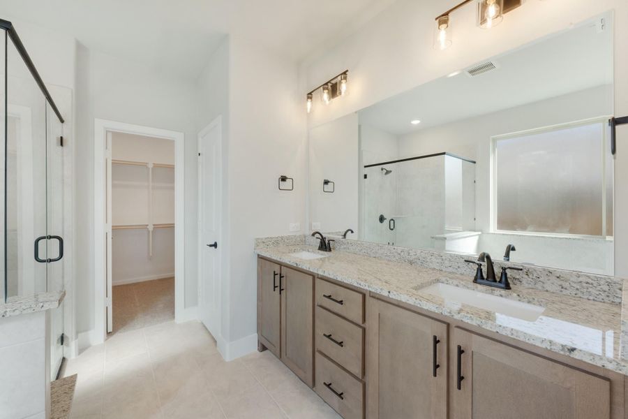 Master bathroom with double vanity, granite countertops, glass shower, and walk-in closet entrance Master bathroom with double vanity, granite countertops, glass shower, and walk-in closet entrance