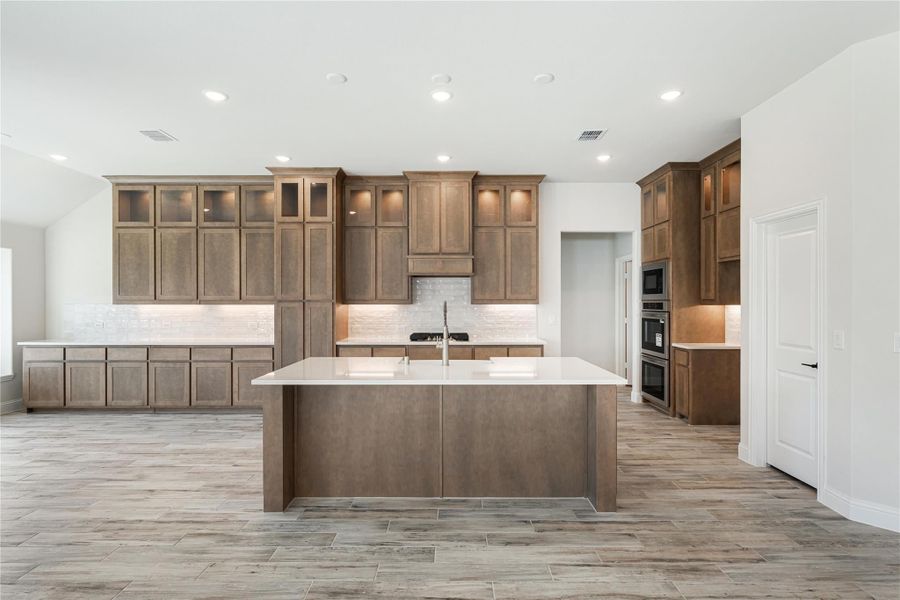 Large kitchen with brown wood cabinets, center island with white countertop, and wood-look tile floors