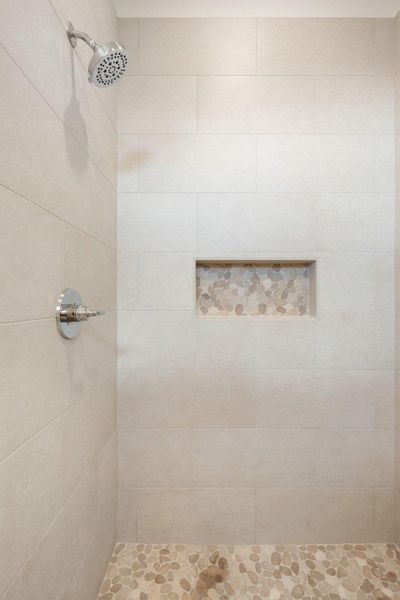 The shower features light-colored tile walls, a built-in niche with pebble mosaic detailing, and a pebble-tiled floor