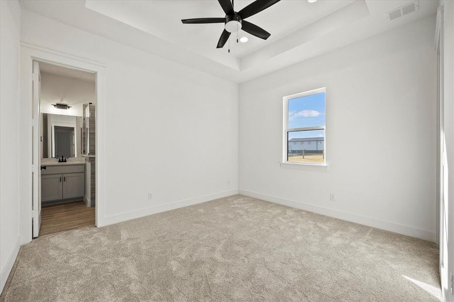 Carpeted spare room featuring ceiling fan and a tray ceiling