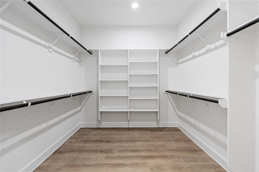 A luxurious walk-in primary closet, designed for maximum organization and style. This expansive space offers a blend of custom-built storage solutions and a sleek, modern design to keep everything effortlessly organized.