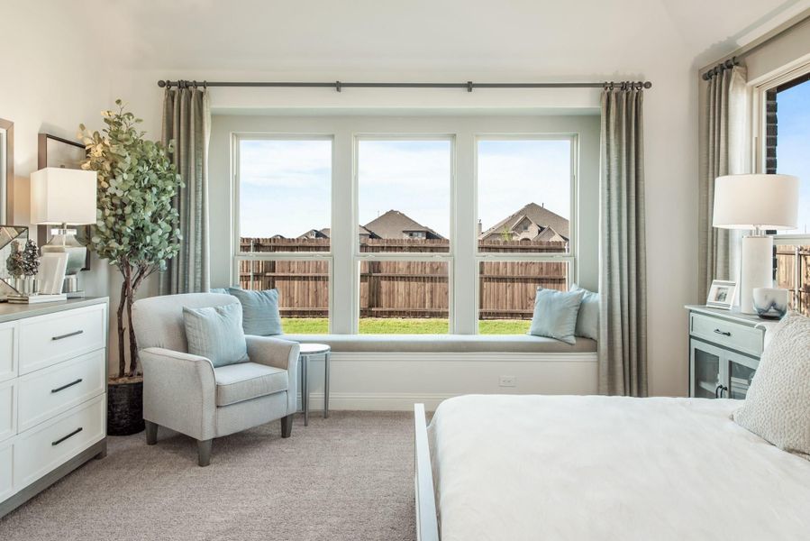 Bedroom with large triple window, built-in window seat, gray armchair, and white dresser on carpet flooring