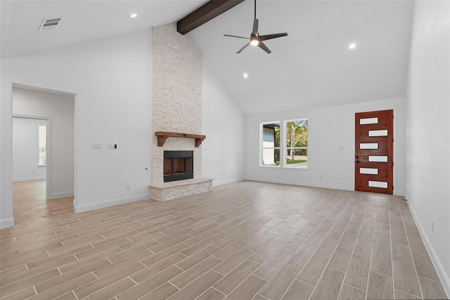 Unfurnished living room with beam ceiling, high vaulted ceiling, a ceiling fan, wood finish floors, and a stone fireplace Unfurnished living room with beam ceiling, high vaulted ceiling, a ceiling fan, wood finish floors, and a stone fireplace