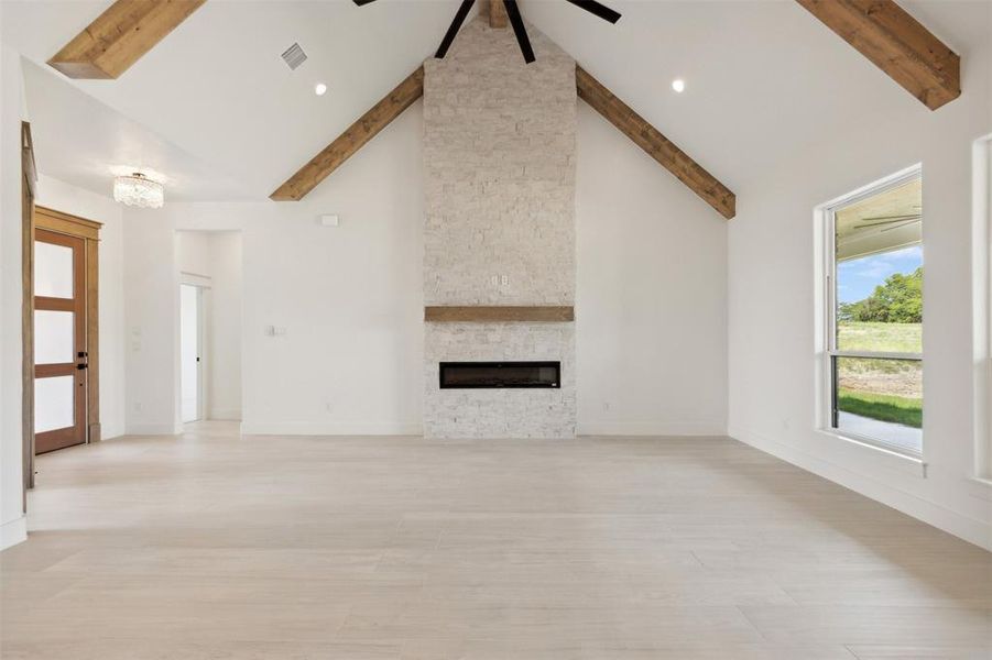 Unfurnished living room featuring high vaulted ceiling, a fireplace, light wood-type flooring, and beam ceiling