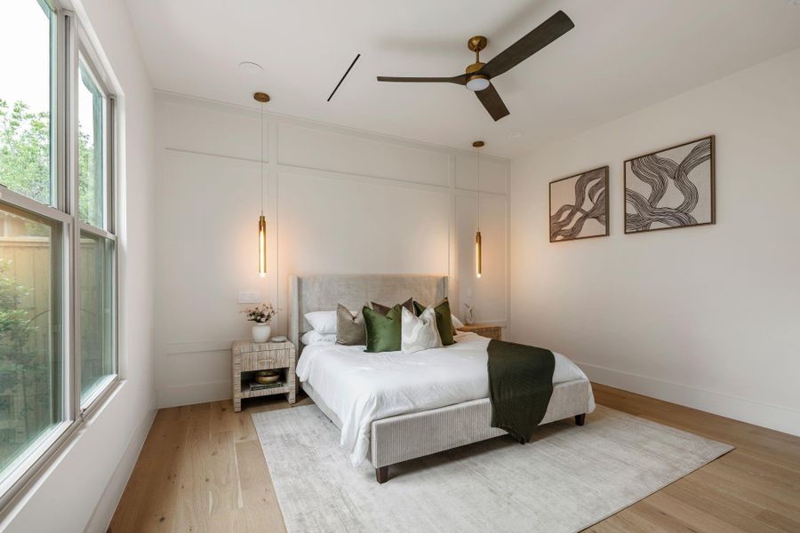 The primary suite offers a serene, light-filled retreat. Subtle panel accent walls, aged brass ceiling fan, and suspended pendant lighting combine to create a calm, refined atmosphere. The primary suite offers a serene, light-filled retreat. Subtle panel accent walls, aged brass ceiling fan, and suspended pendant lighting combine to create a calm, refined atmosphere.