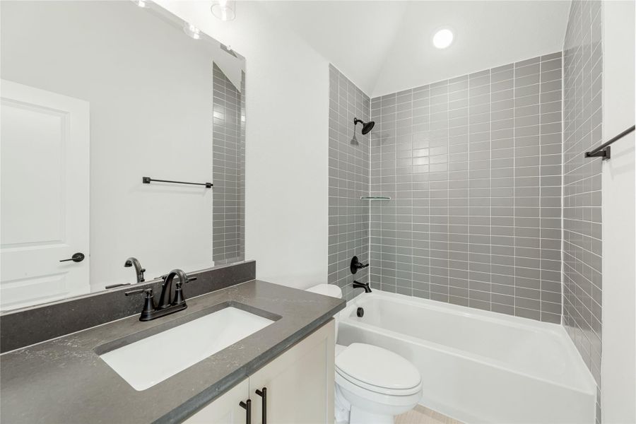 Bathroom with dark countertop vanity, toilet, and tub-shower combo with gray tile surround and black fixtures