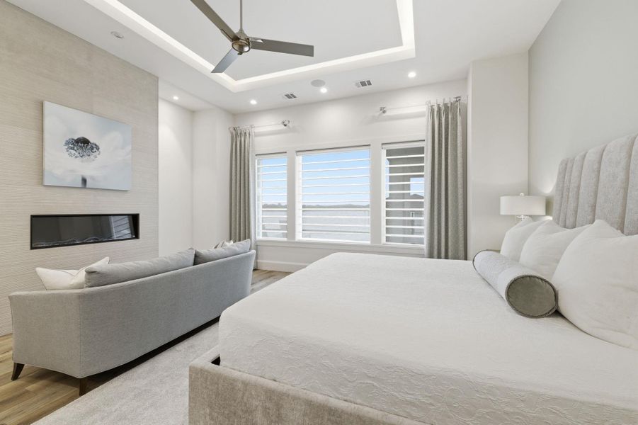Bedroom featuring light wood finished floors, ceiling fan, a fireplace, a tray ceiling, and recessed lighting