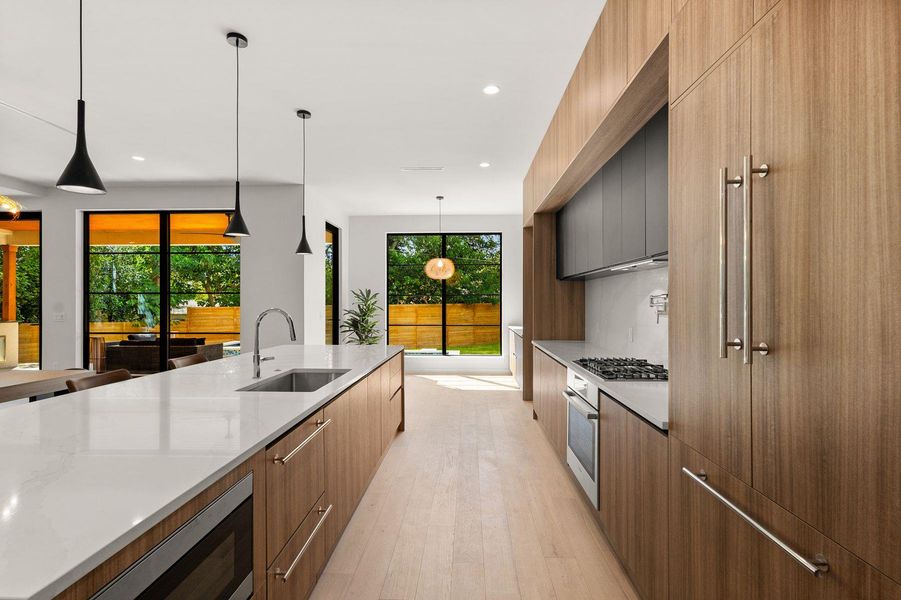 Smooth wood cabinetry and quartz countertops frame this sleek, modern culinary space.