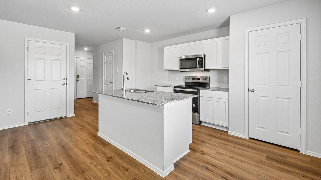 A well-lit kitchen with granite countertops and stainless steel appliances, seamlessly integrating with rich wood flooring.