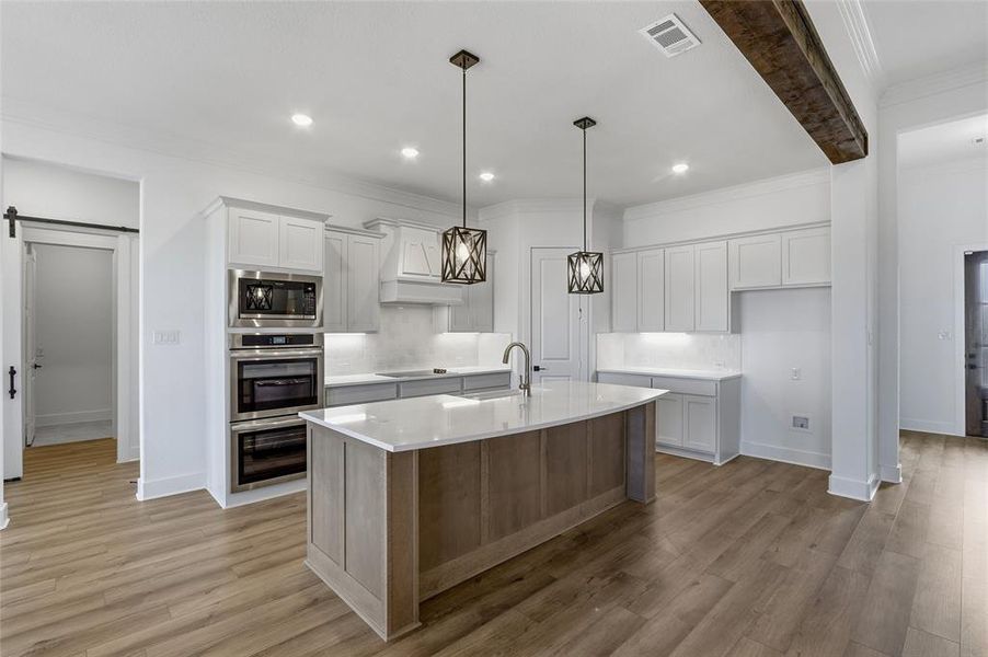 Kitchen featuring a barn door, decorative backsplash, two tone cabinetry, an island with sink, and pendant lighting