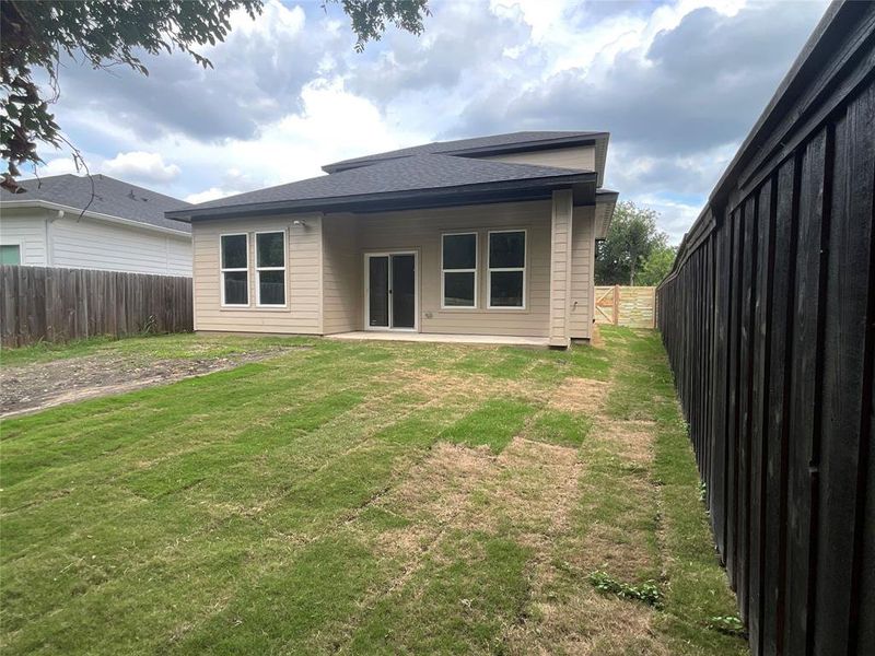 Rear exterior featuring a tan siding facade, black shingle roof, and a concrete patio Rear exterior featuring a tan siding facade, black shingle roof, and a concrete patio