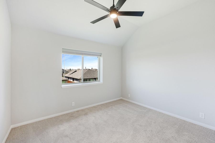 Empty bedroom with vaulted ceiling, black ceiling fan, carpet flooring, and a single window with neighborhood view