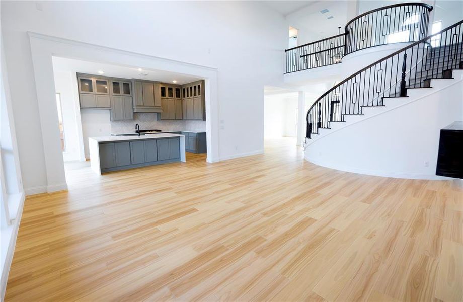 Unfurnished living room with a towering ceiling, light wood finished floors, stairway, and recessed lighting Unfurnished living room with a towering ceiling, light wood finished floors, stairway, and recessed lighting