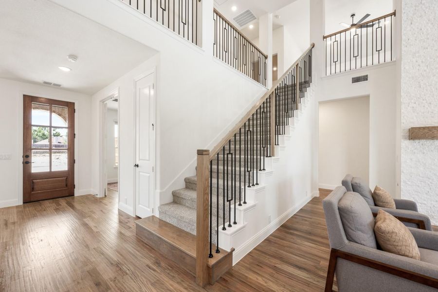 Two-story entryway with carpeted staircase, wood floors, iron balusters, and wood front door