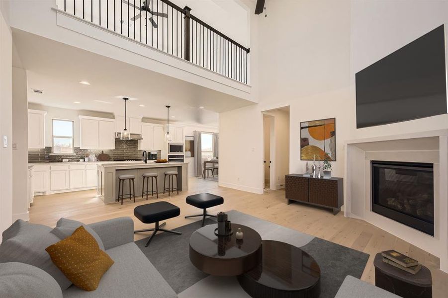 Virtually Staged Photo Living area featuring light wood-type flooring, a glass covered fireplace, recessed lighting, and a towering ceiling
