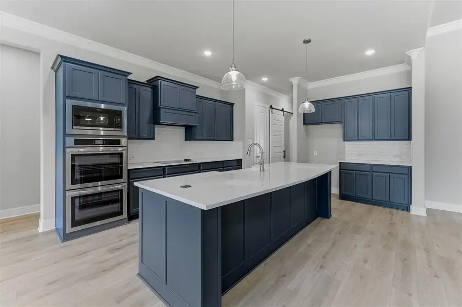 Kitchen featuring dark blue cabinetry, light wood-finish flooring, a white countertop island with a gooseneck faucet, stainless steel double wall ovens, and a subway tile backsplash