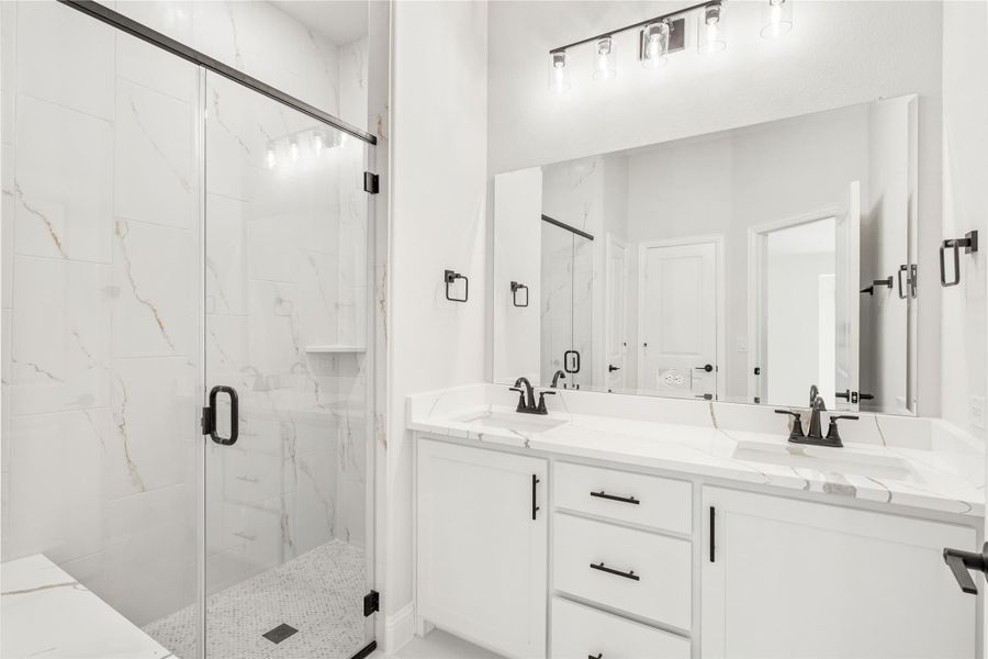 Bathroom with double vanity, white quartz countertops, and glass-enclosed marble tile shower with black hardware