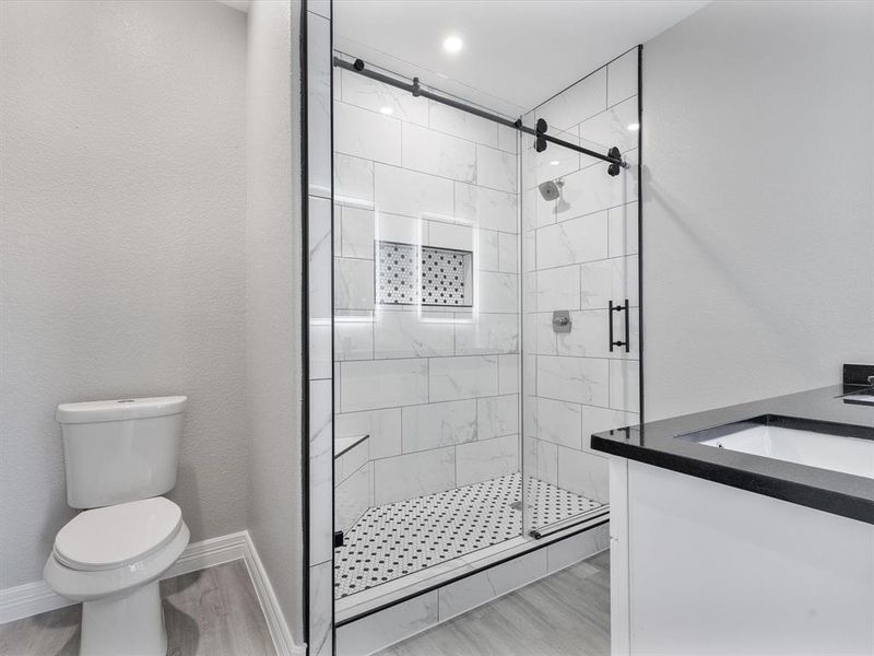 Bathroom with toilet, a shower stall, wood finished floors, and a sink Bathroom with toilet, a shower stall, wood finished floors, and a sink