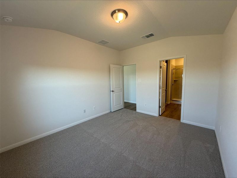 Unfurnished bedroom with vaulted ceiling, carpet floors, and ensuite bathroom