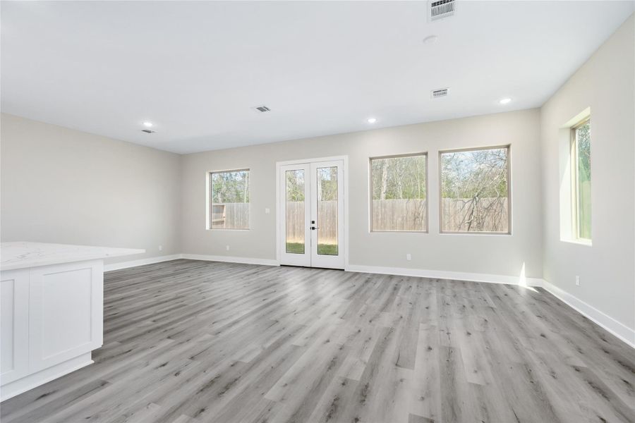 The spacious living space features luxury vinyl plank flooring, neutral walls, and large windows. The welcoming and airy atmosphere is enhanced by the beauty of natural light flooding the room.