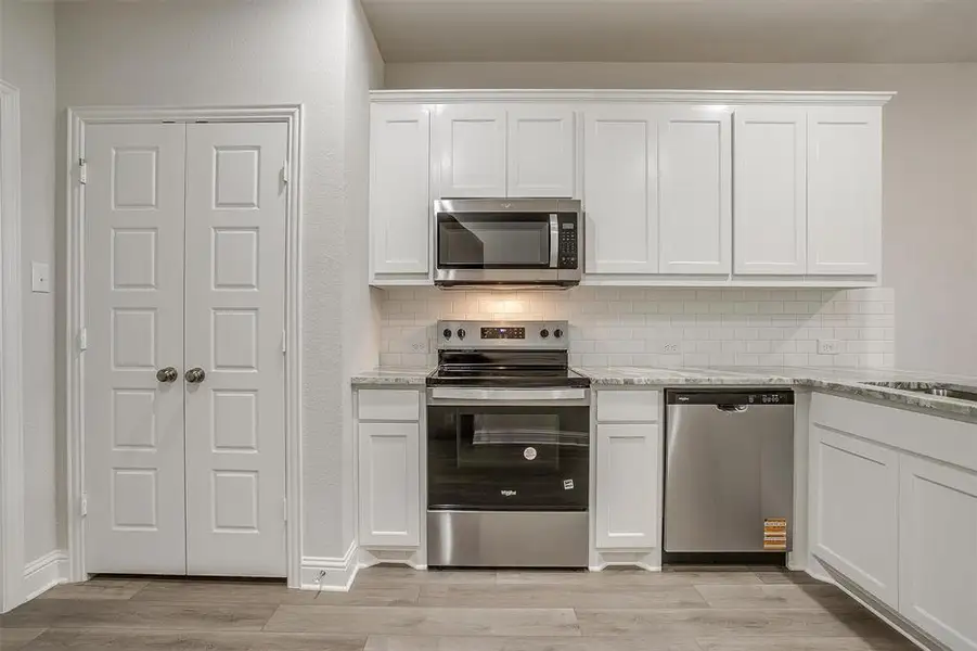 Kitchen featuring stainless steel appliances, backsplash, white cabinets, and light stone counters
