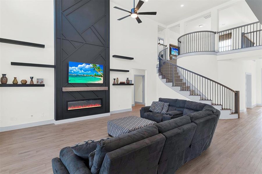 Living area with a fireplace, a towering ceiling, light wood finished floors, stairs, and a ceiling fan Living area with a fireplace, a towering ceiling, light wood finished floors, stairs, and a ceiling fan