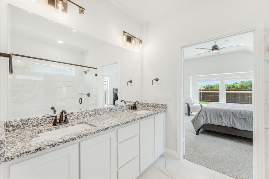 Ensuite bathroom with double vanity, granite countertops, white cabinets, and glass shower, open to master bedroom.