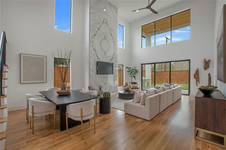 Living room with a fireplace, a high ceiling, light hardwood / wood-style floors, and ceiling fan