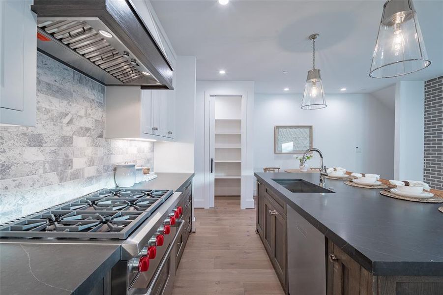 Kitchen with custom exhaust hood, appliances with stainless steel finishes, hanging light fixtures, and decorative backsplash