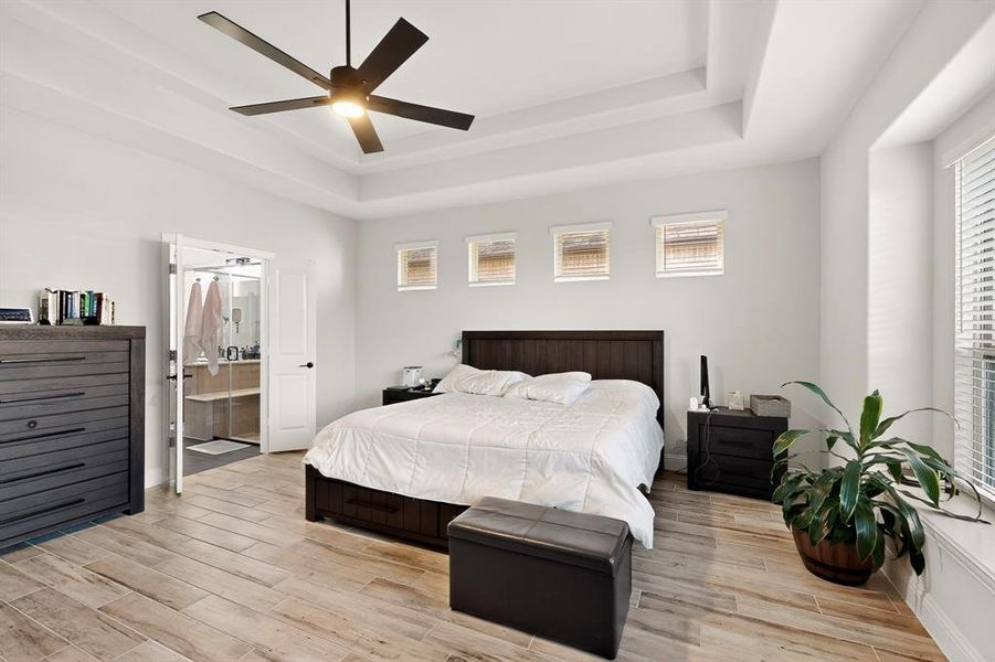 Bedroom with wood tiled floors, a tray ceiling, a ceiling fan, and connected bathroom Bedroom with wood tiled floors, a tray ceiling, a ceiling fan, and connected bathroom