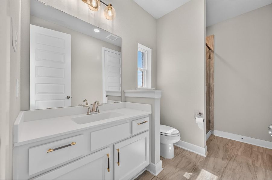 Gorgeous secondary bathroom with a quartz-topped vanity, stylish gold hardware, and wood-look tile flooring. A private water closet and walk-in shower complete this bright, functional space.