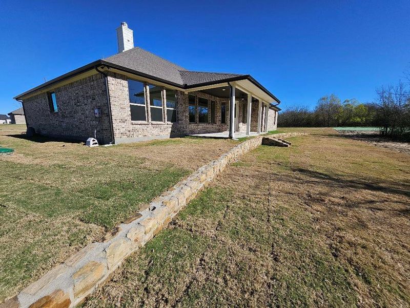 Rear view of house with a patio area, a yard, brick siding, a chimney, and a shingled roof