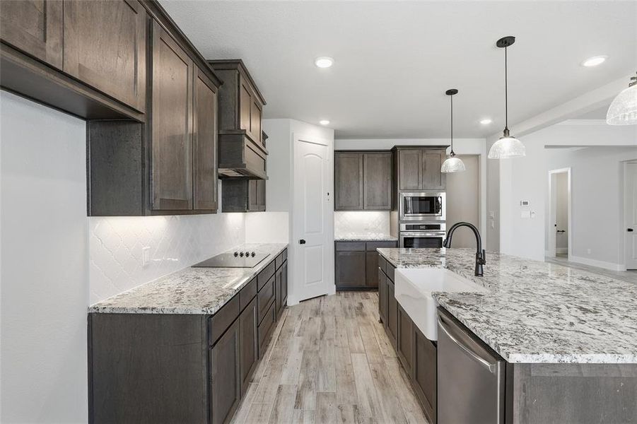Kitchen with dark brown cabinets, light stone countertops, light wood-style floors, an island with sink, and stainless steel appliances