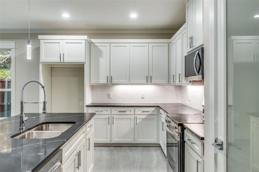 Kitchen featuring sink, stainless steel appliances, hanging light fixtures, and white cabinets