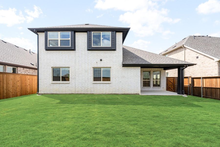 Two-story white brick home rear view with covered patio, green lawn, and wood privacy fence
