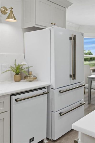The kitchen features white cabinetry, a white dishwasher, and a white refrigerator with dark-toned hardware The kitchen features white cabinetry, a white dishwasher, and a white refrigerator with dark-toned hardware
