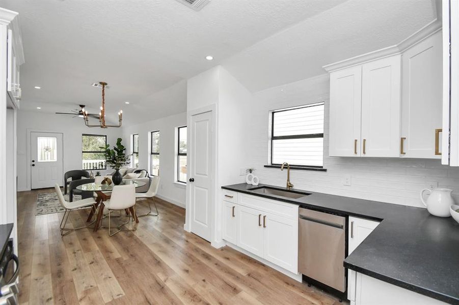 This photo showcases a modern kitchen with white cabinetry, dark countertops, stainless steel appliances, and a white subway tile backsplash. It features sleek gold hardware and a well-lit window.