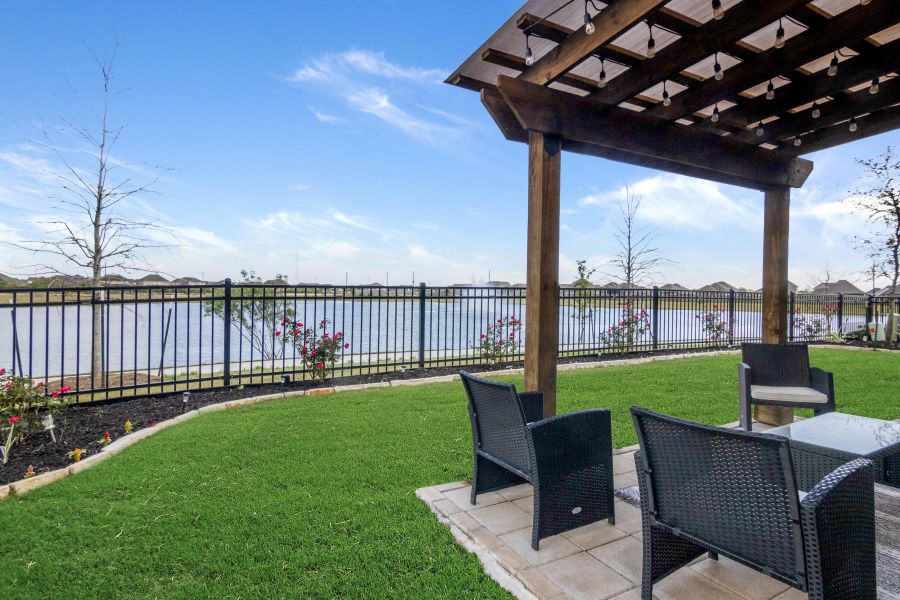 This backyard offers a serene lakeside view, featuring a patio with a wooden pergola. The space is enhanced by a well-kept lawn and tasteful landscaping, perfect for relaxation and outdoor gatherings.