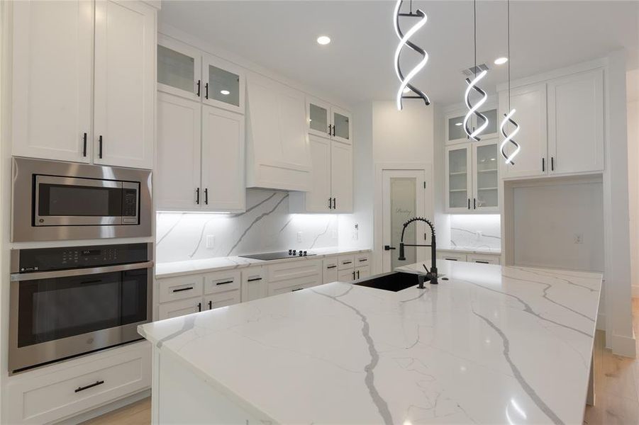 Kitchen with glass insert cabinets, light stone countertops, stainless steel appliances, white cabinets, and recessed lighting