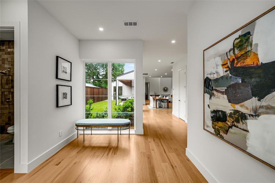 Hardwood flooring extending through the hallway, recessed lighting, and white baseboards