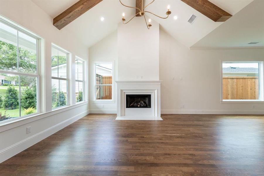 Spacious room featuring vaulted ceilings with exposed wood beams, a white mantel fireplace, and wood-finish flooring Spacious room featuring vaulted ceilings with exposed wood beams, a white mantel fireplace, and wood-finish flooring
