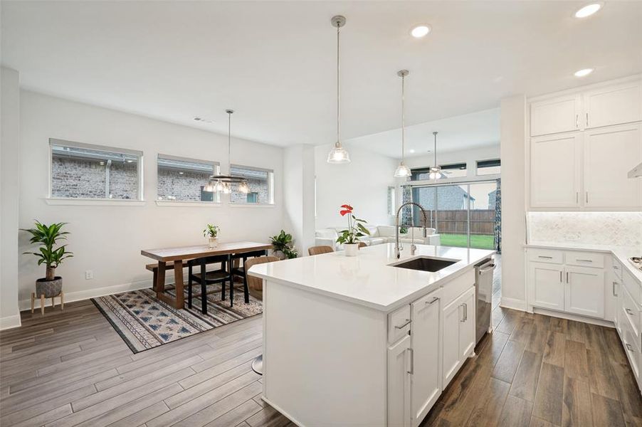 Open-concept kitchen and dining area featuring a spacious island with an integrated sink, white cabinetry, wood-finish flooring, and a sliding glass door leading to the backyard