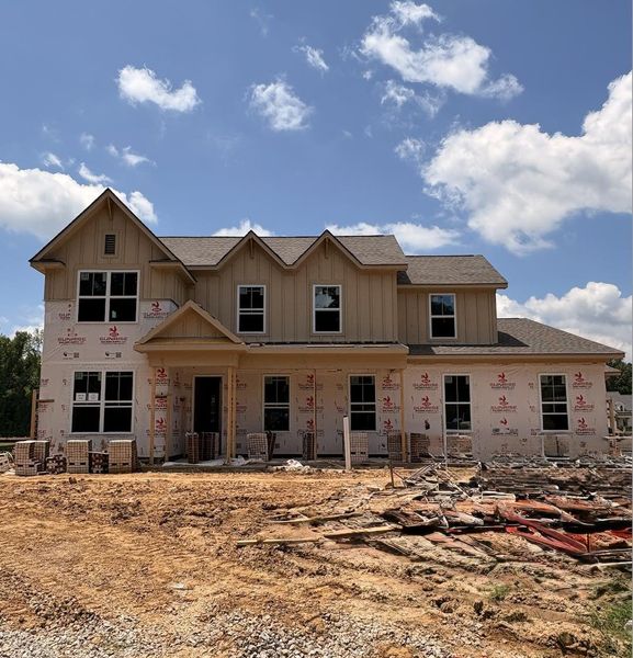 Two-story residential structure under construction featuring gabled rooflines, vertical board and batten siding, multiple window openings, and a covered front entry Two-story residential structure under construction featuring gabled rooflines, vertical board and batten siding, multiple window openings, and a covered front entry